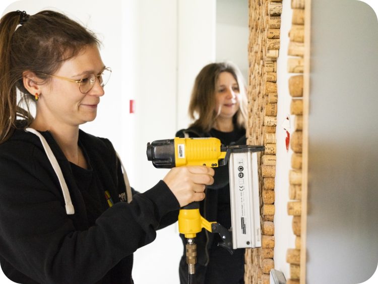 Medewerkster van Upgrade Estate bevestigt gerecycleerde wijnkurken op een muur als onderdeel van de look & feel-upcycling in een project.