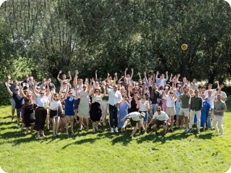 Groepsfoto van alle medewerkers van Upgrade Estate die juichend in de lucht springen op een zonnige dag in het groen.